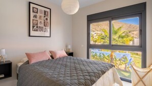 A bedroom with a large bed, a framed picture on the wall, and a window with a view of palm trees. - Alegría Village by Interhome (Benidorm)