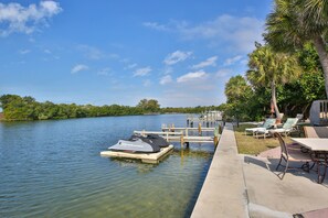Une jetée avec un jet ski et des chaises longues, au bord d’un lac paisible, le tout entouré de verdure.
