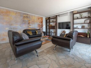 Uma sala de estar moderna com dois sofás de couro, piso de ladrilho de pedra, uma grande pintura abstrata e estantes embutidas com objetos decorativos.