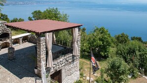Un espacio de estar al aire libre con construcción de piedra y vistas al mar y montañas lejanas.