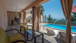 Un balcón con piscina, mobiliario exterior y vista al mar.