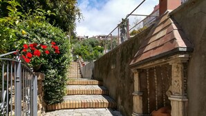 Un corridoio esterno stretto con gradini in mattoni che conducono a una porta con una colonna in pietra e un piccolo portico.