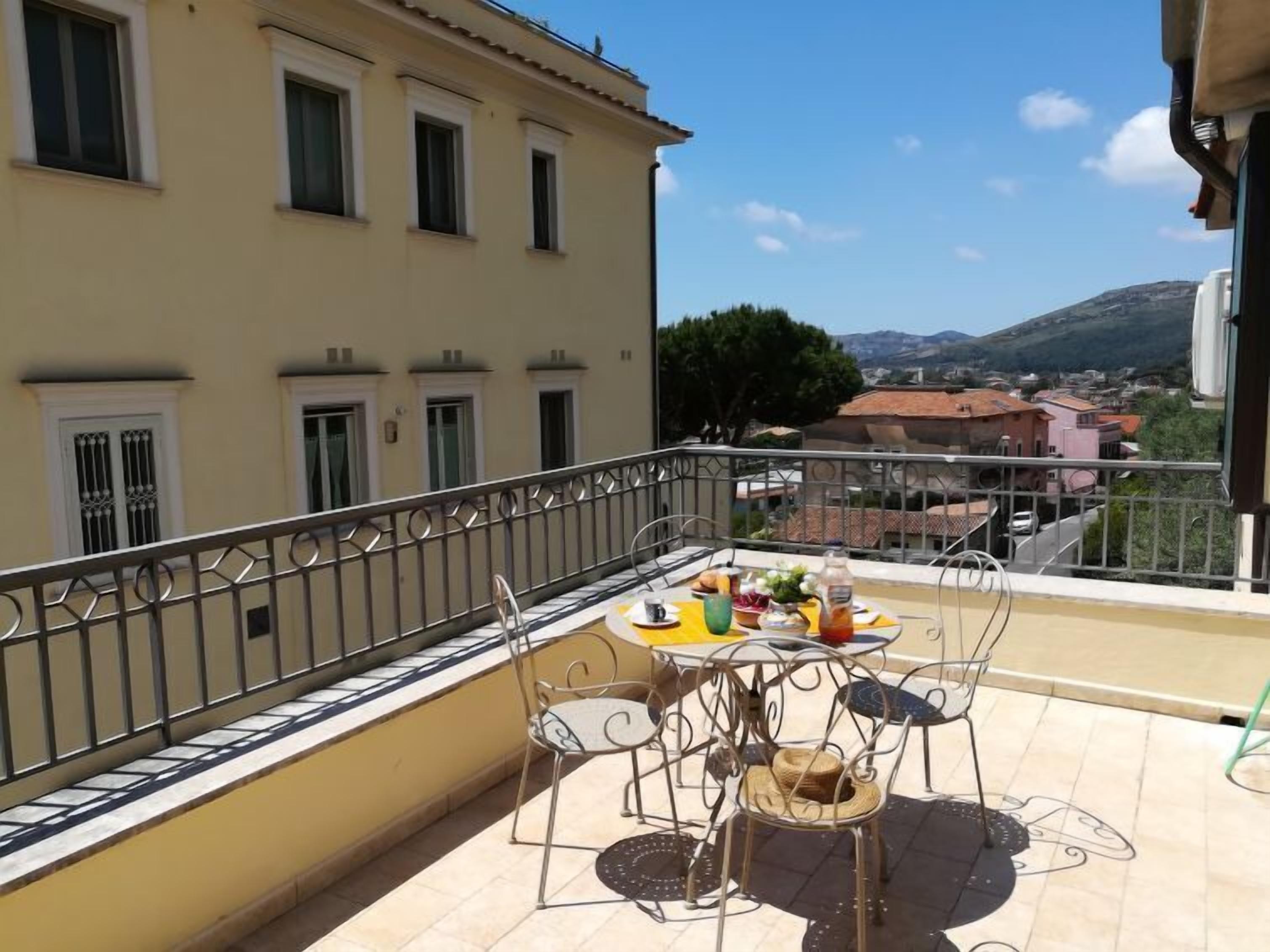 A balcony with a table set for two, overlooking a town and hills.