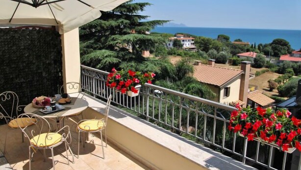 Un balcone con un tavolo, sedie, un ombrellone bianco e fiori rossi.