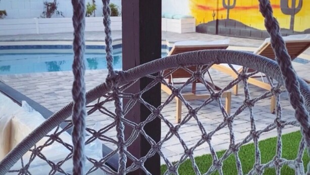 A pool area with a rope chair, lounge chairs, and a mural of cacti. - Modern Living with an Outdoor Oasis (Scottsdale)