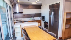 Une cuisine moderne avec une table à manger en bois, des appareils électroménagers intégrés et un grand réfrigérateur.