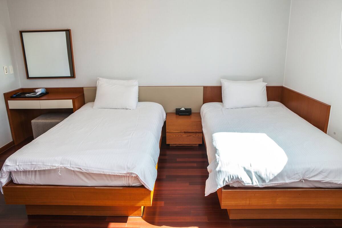 A twin room with two single beds, a wooden desk, a chair, and a small bedside table with a lamp.