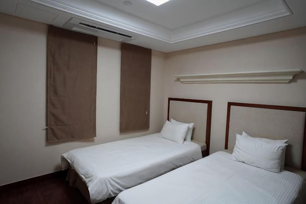 Une chambre d’hôtel avec deux lits simples, un ventilateur de plafond et une fenêtre avec des stores.
