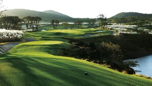 Un parcours de golf avec un plan d’eau, des arbres et des collines en arrière-plan.