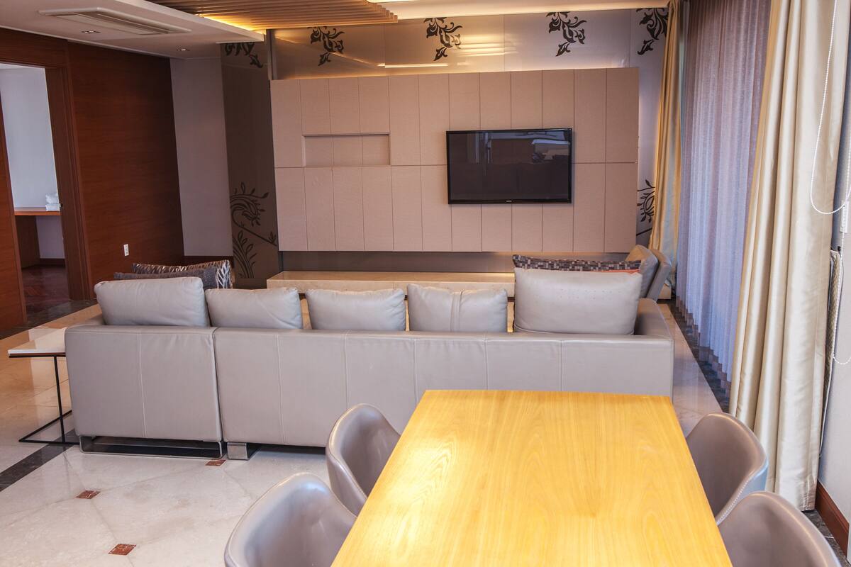 A modern living room with a sofa, a wooden table, and a flat-screen TV mounted on the wall.