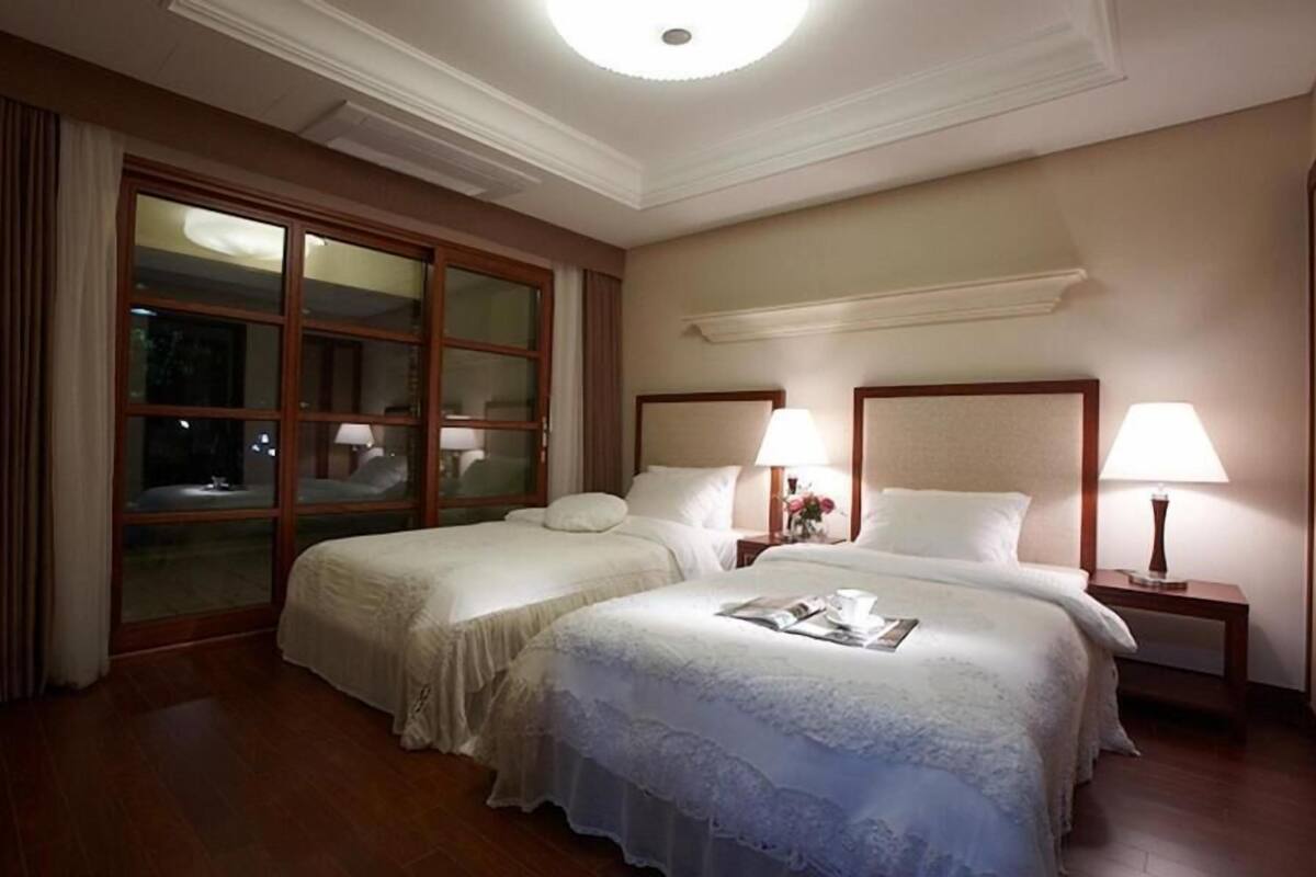 A hotel room with two beds, a large window, and a nightstand with a lamp.