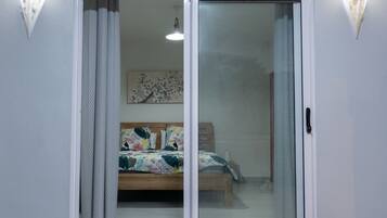 Une chambre avec une porte-fenêtre coulissante, un lit avec une literie à motifs floraux et un luminaire fixé au mur.