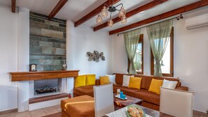 A living room with a fireplace, a sofa set, a wooden coffee table, and a dining table. - Evilion Villa (gennadi)