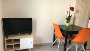 Ein kleines Zimmer mit Fernseher auf einem Schrank, zwei orangefarbene Sessel, einem Tisch und einer Topfpflanze.