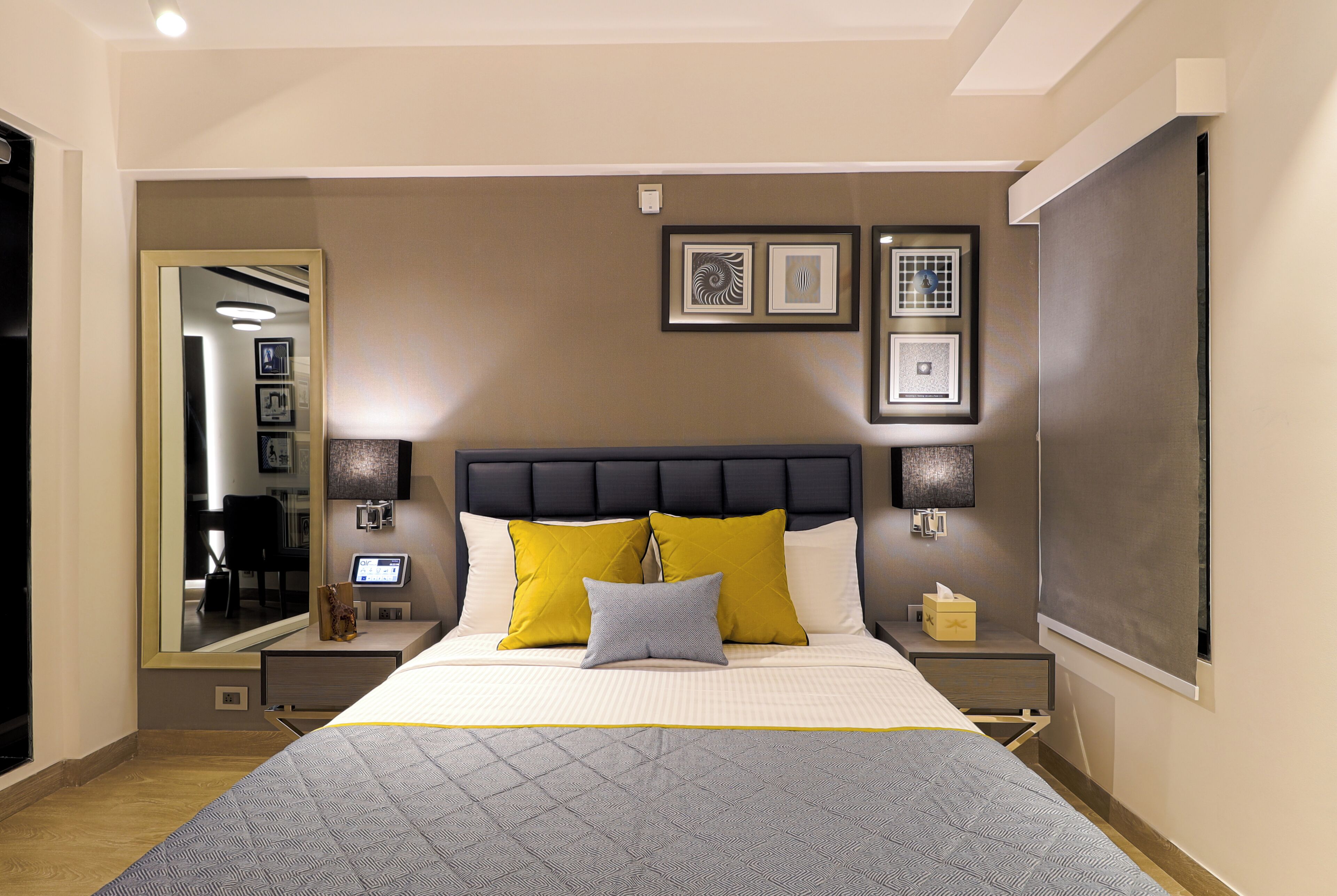 Una habitación de hotel moderna con una cama grande, una mesita de noche, un espejo y obras de arte enmarcadas en la pared.