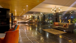 A modern lobby with a wooden ceiling, glass walls, a sofa, and orange chairs. - AIR by Ahuja Residences (Gurugram)
