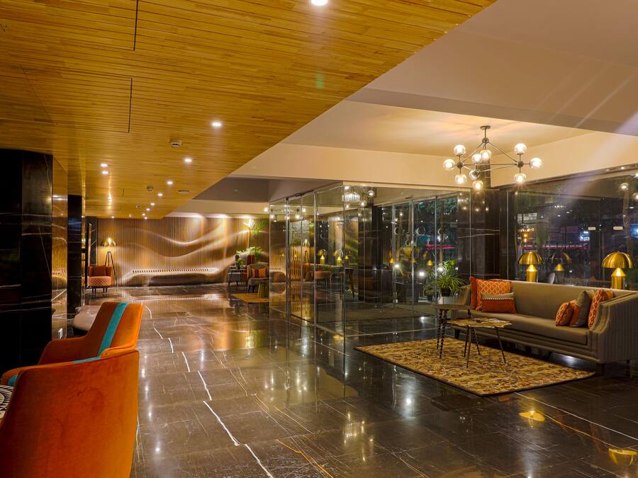 Un vestíbulo moderno con techo de madera, paredes de vidrio, un sofá y sillones naranjas.