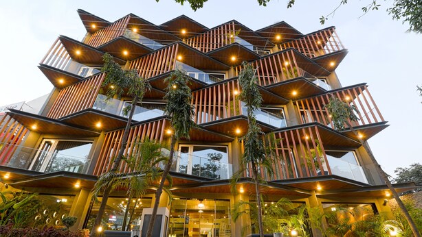 A modern multi-story building with a unique angular design, featuring balconies with plants and warm lighting. - AIR by Ahuja Residences (Gurugram)