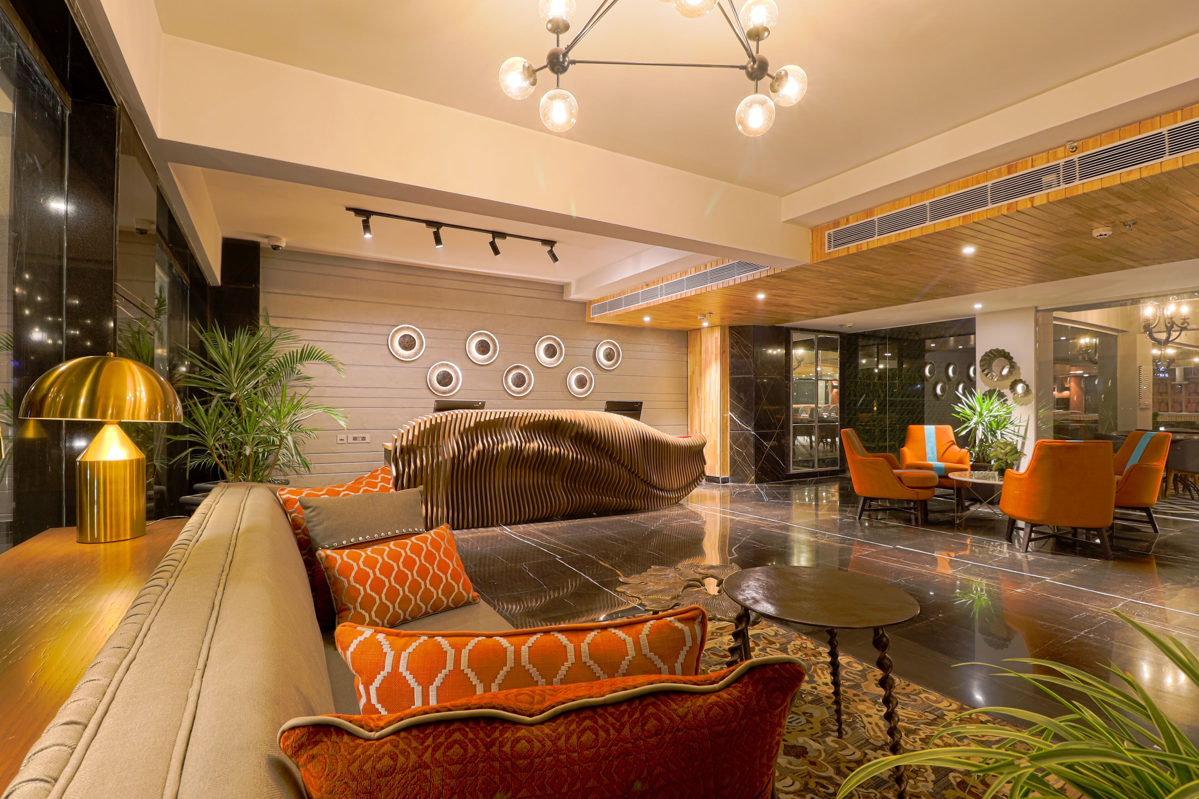 A modern lobby with a sofa, orange chairs, a chandelier, and a patterned rug.