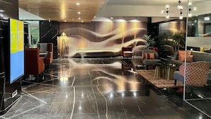 A modern lobby with a reflective floor, seating areas, and a unique textured wall. - AIR by Ahuja Residences (Gurugram)