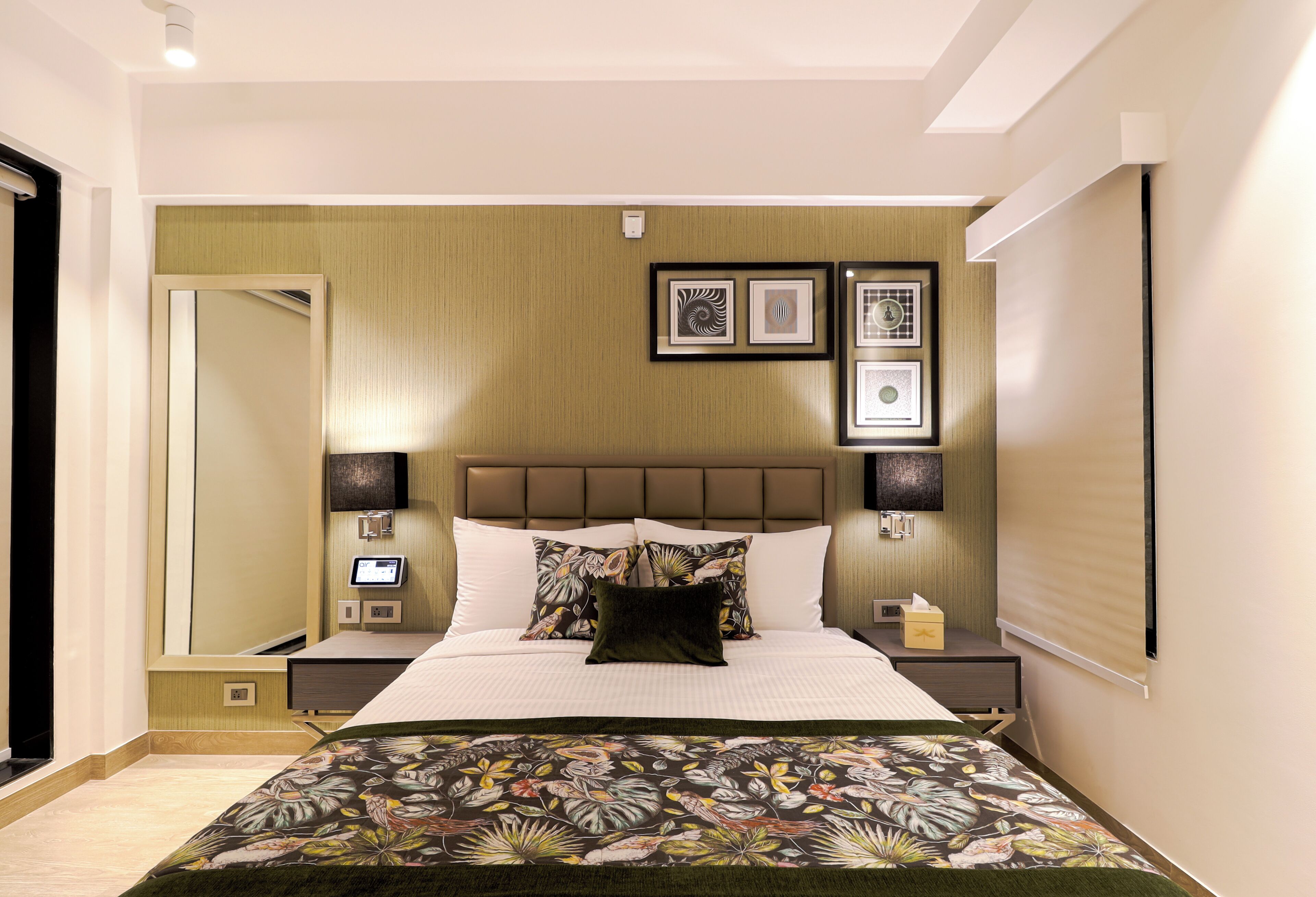 A modern hotel room with a large bed, a headboard with built-in lighting, a bedside table with a lamp, and framed artwork on the wall.