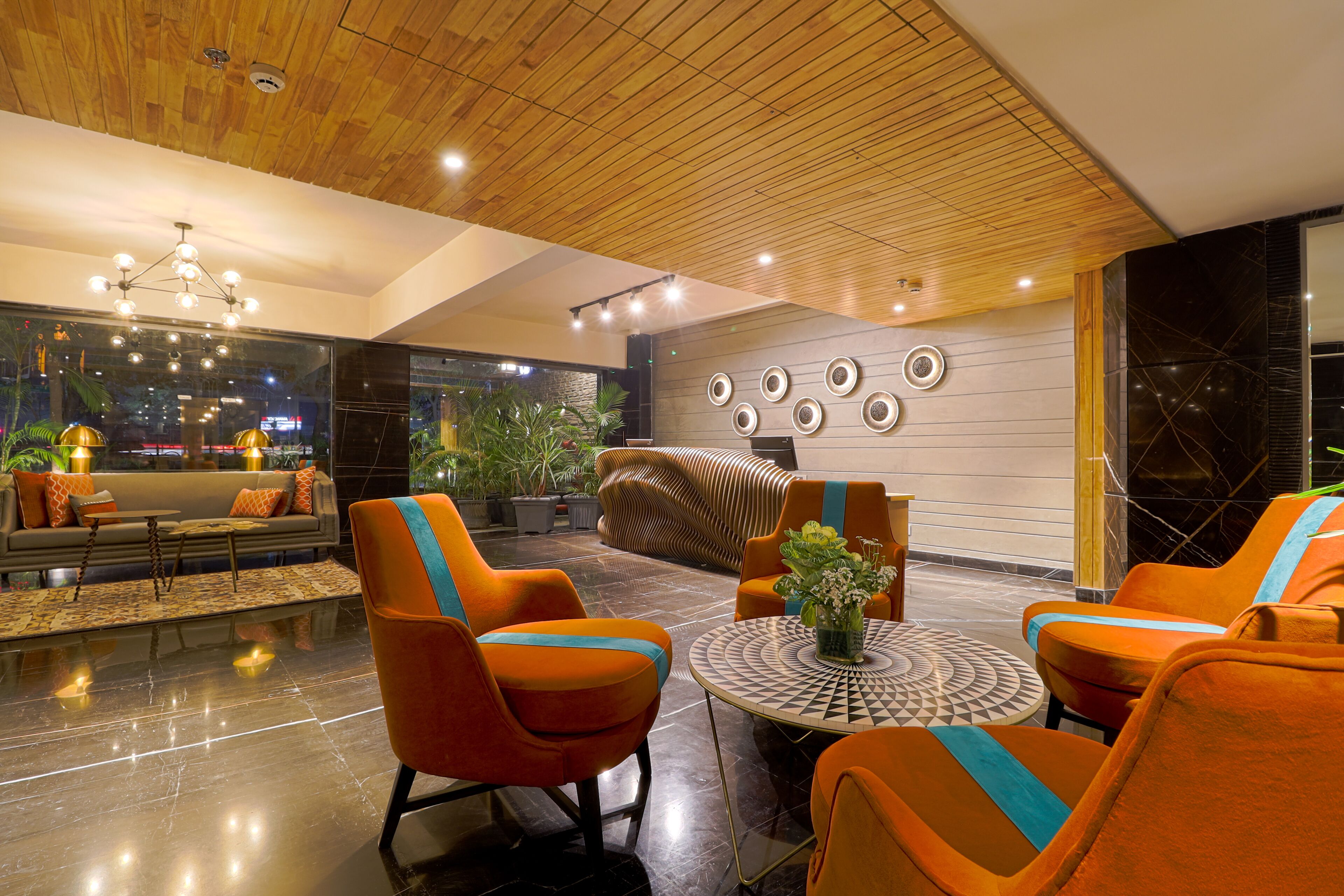 Eine moderne Lobby mit orangefarbenen Sesseln, einem runden Tisch und einer Holzbalkendecke.