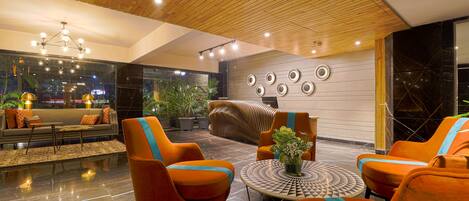Eine moderne Lobby mit orangefarbenen Sesseln, einem runden Tisch und einer Holzbalkendecke.