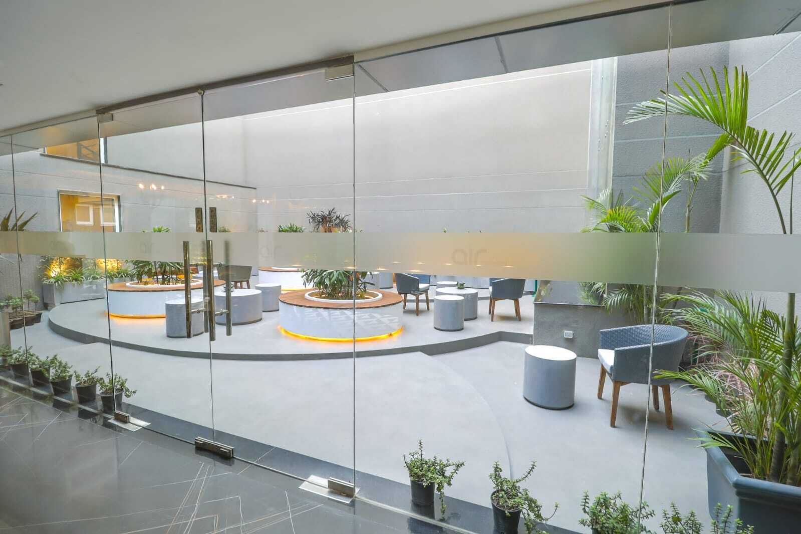 Amplio espacio interior con una zona de estar central, rodeado de plantas en macetas y muebles modernos.
