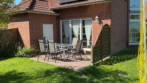 A brick house with a tiled roof, solar panels, a patio with a table and chairs, and a gated entrance. - Vacation home in Nessmersiel 20-007a - 200-007a (Dornum)