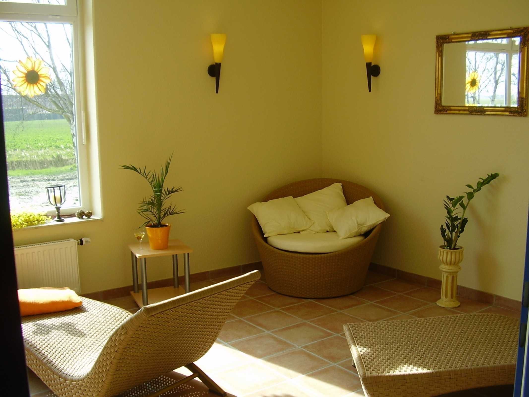 Una habitación con una silla de mimbre, un sofá redondo de mimbre con cojines, una mesita con una planta y dos lámparas fijadas a la pared.