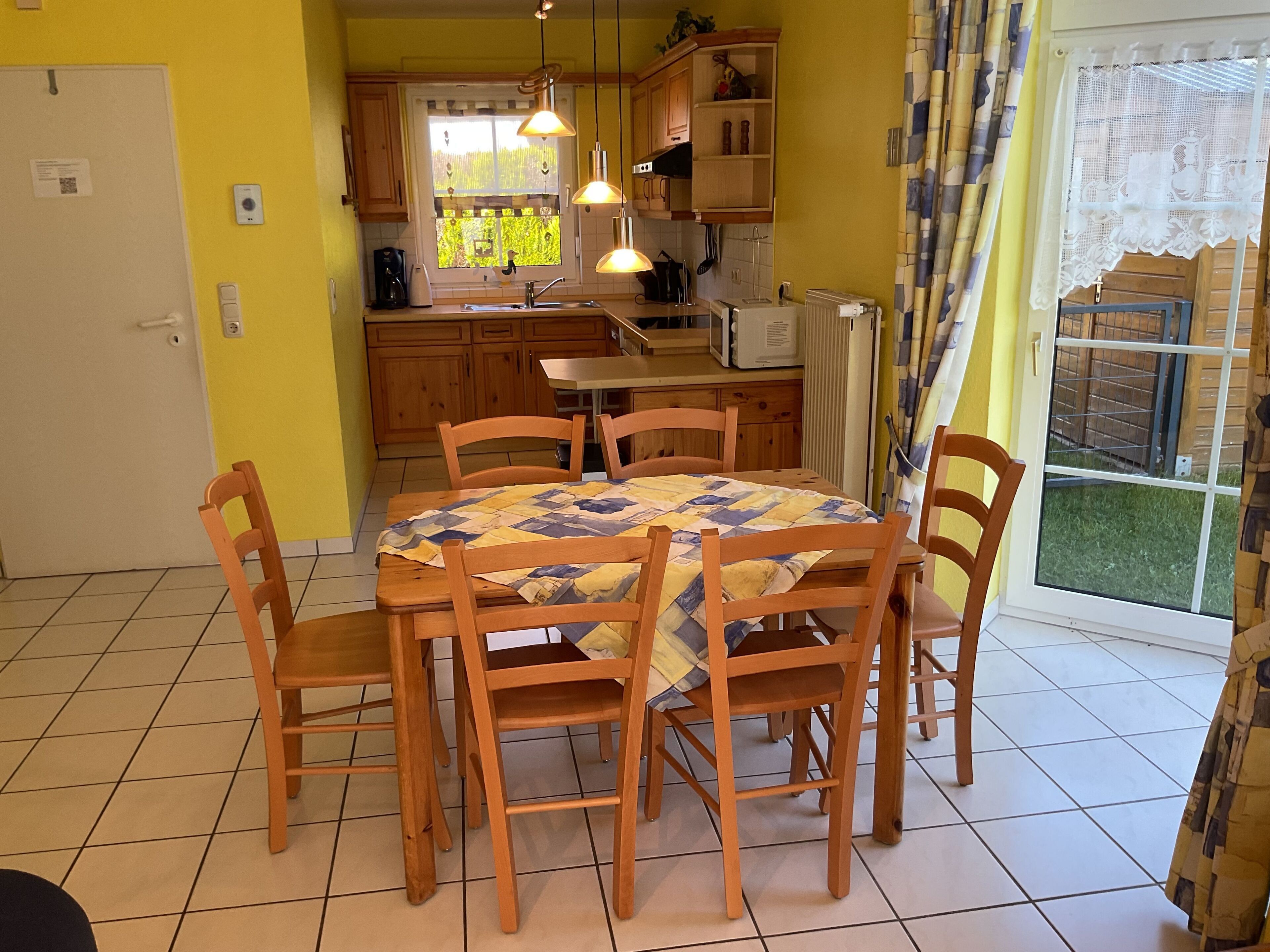 A dining area with a table set for six, surrounded by wooden chairs, in a room with yellow walls and a large window.