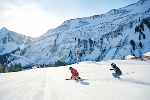 A ski slope with a chairlift, skiers, and snow-covered mountains.