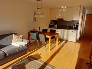A modern living room with a sofa, dining table, chairs, and a kitchen area with cabinets and appliances.