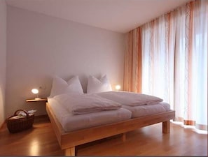 A bedroom with a wooden bed, bedside lamps, a nightstand, and a window with curtains.