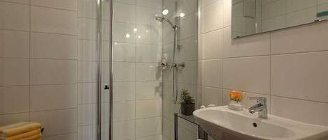 Un baño moderno con ducha de vidrio, un lavabo con espejo y un perchero para toallas.