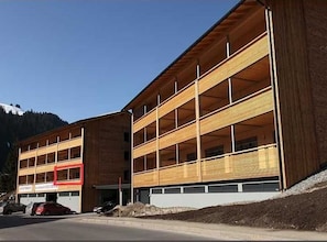A multi-story building with a wooden facade, a garage, and a parking area.