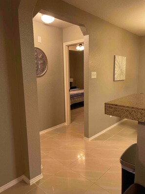 A hallway with a door leading to a bedroom, a small bathroom, and a kitchen area with a countertop.