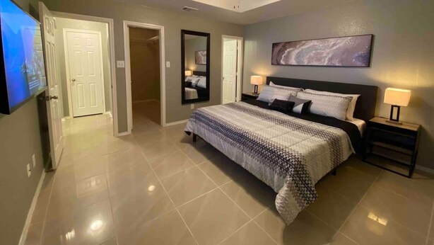 A bedroom with a bed, nightstands, a ceiling fan, a large mirror, and a TV. - Cozy 3BR 2BA Longhorn Creek Retreat Near JW Marriott with Fenced Yard (San Antonio)