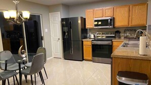 A modern kitchen with a dining area, featuring stainless steel appliances, wooden cabinets, and a glass dining table with chairs. - Cozy 3BR 2BA Longhorn Creek Retreat Near JW Marriott with Fenced Yard (San Antonio)