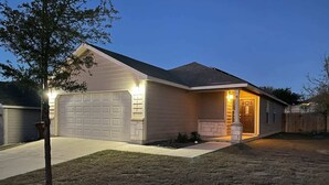 A residential house with a garage, a driveway, and a well-lit entrance. - Cozy 3BR 2BA Longhorn Creek Retreat Near JW Marriott with Fenced Yard (San Antonio)