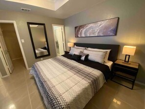A bedroom with a large bed, two bedside tables with lamps, a wall-mounted mirror, and a galaxy-themed painting.