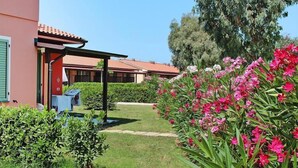 Un jardin agrémenté d’un belvédère, un bâtiment avec un toit rouge et des fleurs roses.