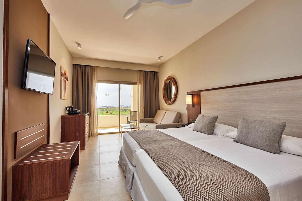 A hotel room with a bed, a TV, a desk, and a balcony with a view.