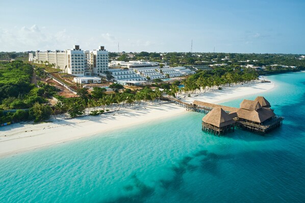 An aerial view of a resort with overwater bungalows, a beach, and a hotel complex.