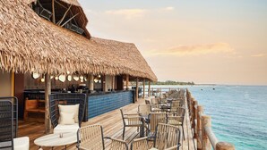 Un restaurant en bord de mer, doté d’un toit de chaume, d’une terrasse en bois et de tables en plein air offrant une vue sur l’océan.