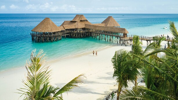 Des bungalows sur pilotis avec toits de chaume, une plage de sable fin et une eau turquoise cristalline.