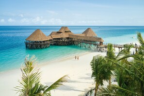 Overwater bungalows with thatched roofs, a sandy beach, and clear turquoise water.