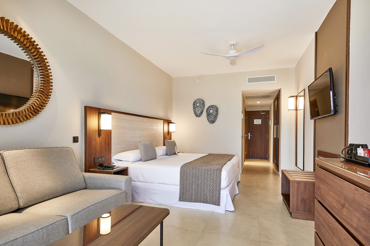 A hotel room with a bed, a sofa, a TV, and a desk.