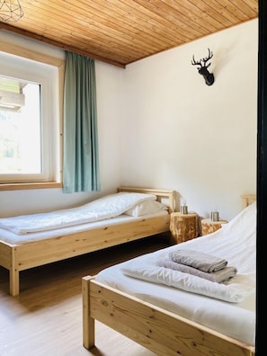 Une pièce avec deux lits superposés en bois, une fenêtre avec des rideaux, une décoration murale représentant une tête de cerf et une petite table de chevet avec une lampe.