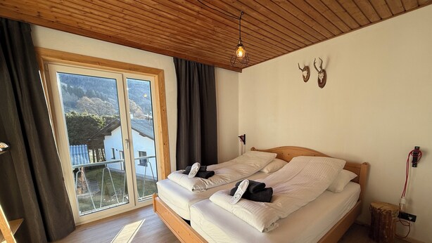 Una cama doble con sábanas blancas, techo de madera y vistas al exterior a través de una puerta corrediza.